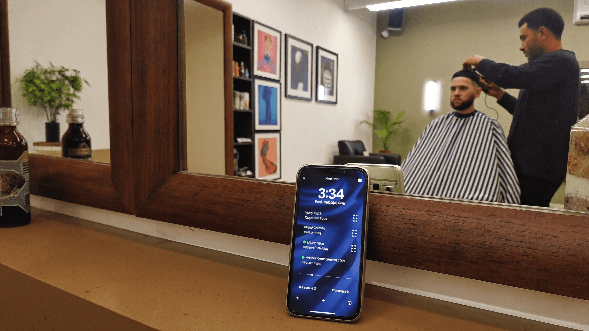 Interior de barbearia moderna com barbeiro atendendo cliente e celular mostrando a agenda no balcão