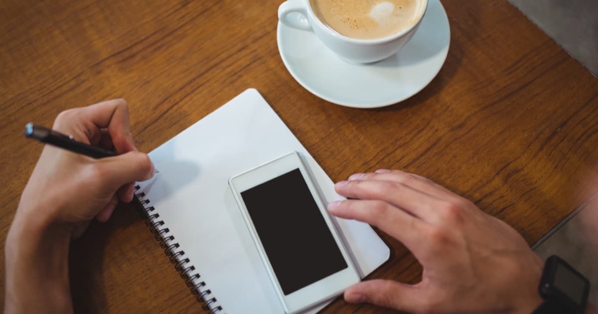 Dono de negócio anotando contatos no caderno com o celular na mão